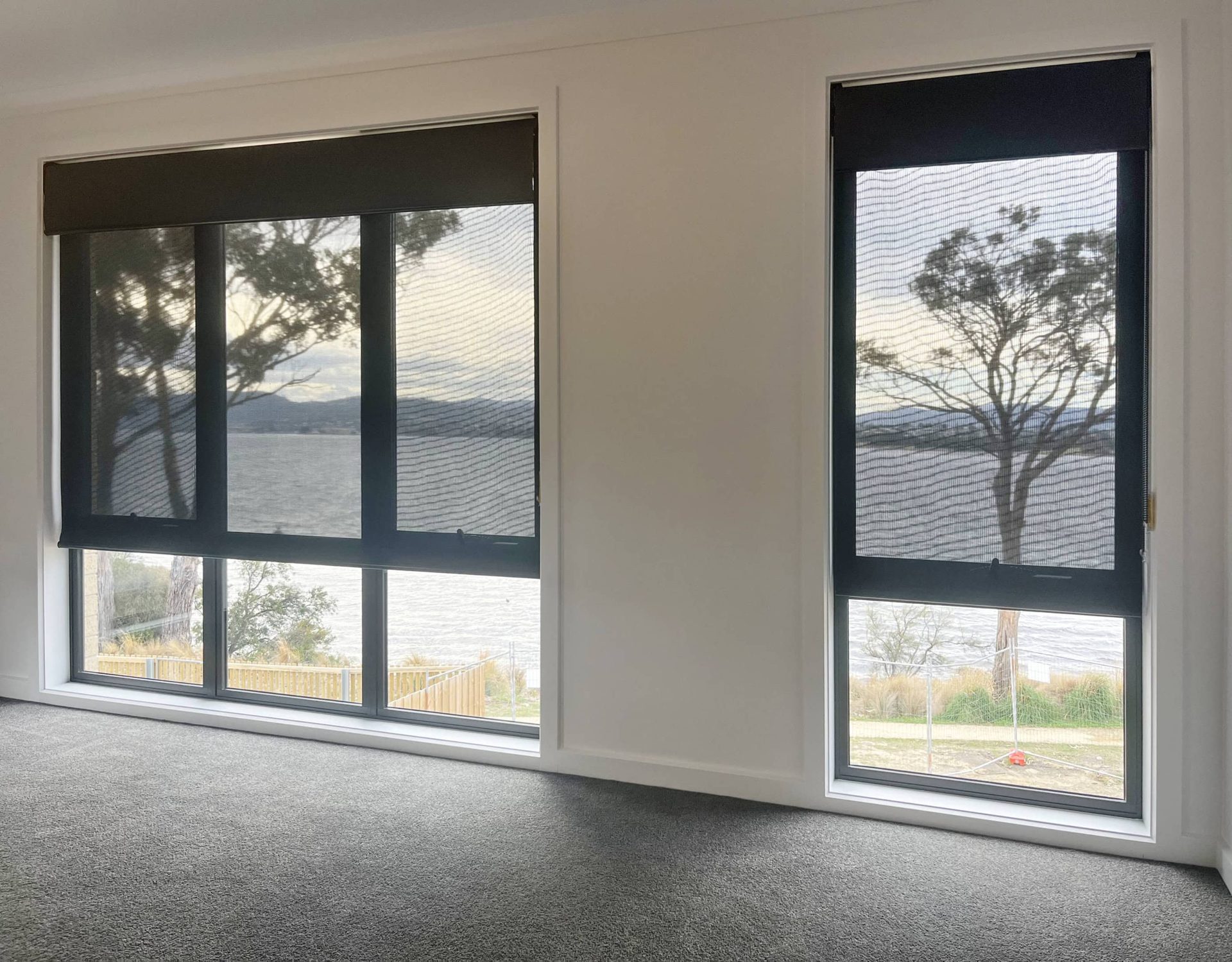 Dual roller blinds across a wall of windows looking out over the water