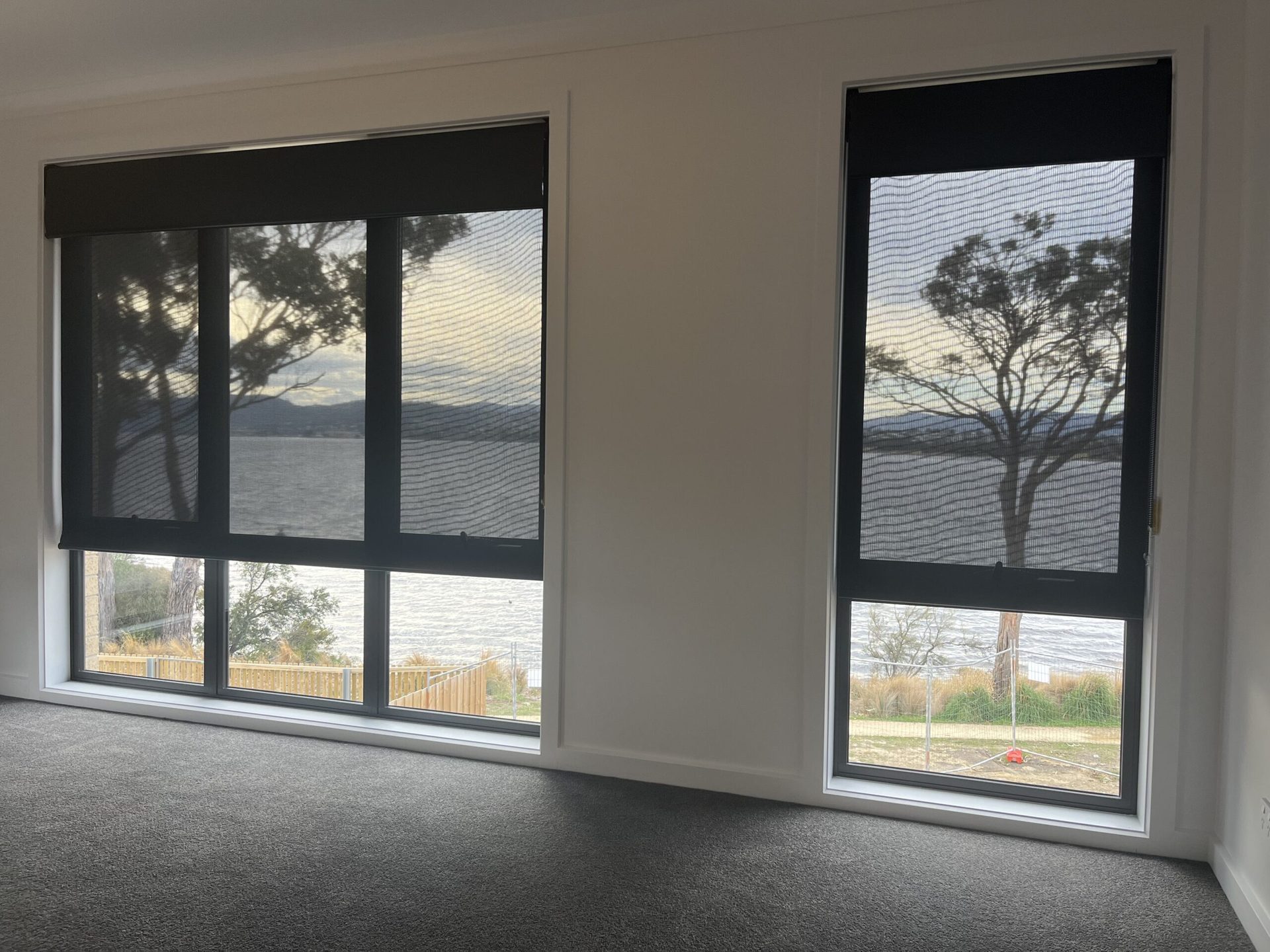 Sunscreen roller blinds over sliding doors with a water view beyond
